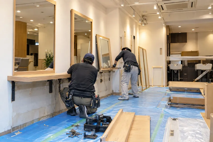 閉店後の美容室で、壁に固定されたセット面の鏡を取り外す職人